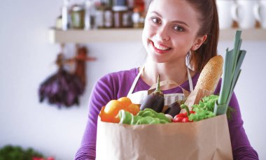 Mutfakta elinde bir torba erzakla duran genç bir kadın..