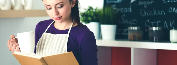 Mujer joven leyendo libro de cocina en la cocina, buscando receta — Foto de Stock