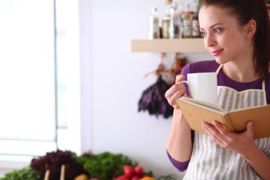 Mutfakta yemek kitabı okuyan genç bir kadın yemek tarifi arıyor.