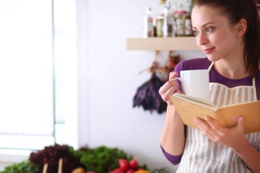 Mutfakta yemek kitabı okuyan genç bir kadın yemek tarifi arıyor.