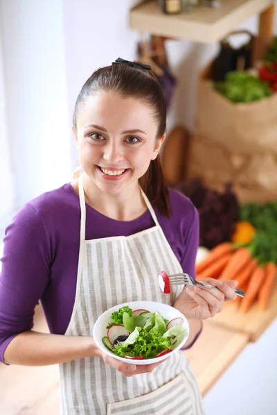 Mujer joven comiendo ensalada fresca en la cocina moderna — Foto de Stock