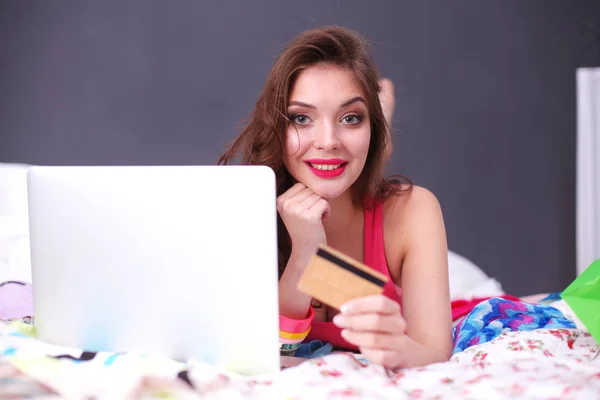 Vacker kvinna liggande på sängen med en laptop och kreditkort — Stockfoto