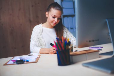 Ofiste çalışan genç bir kadın, masada oturuyor.