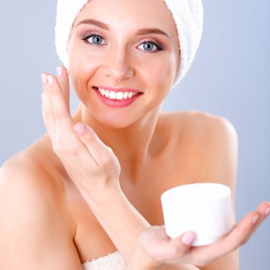 Güzel genç kadın yüzünde gri arka plan üzerinde izole bir krem uygulamak