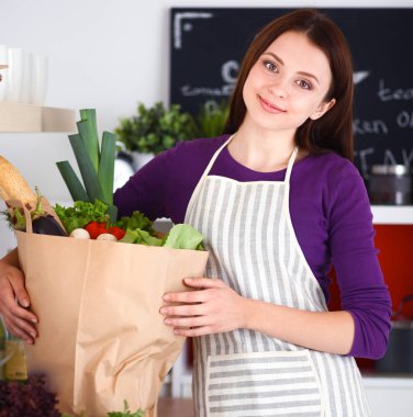 Mutfakta elinde bir torba erzakla duran genç bir kadın..