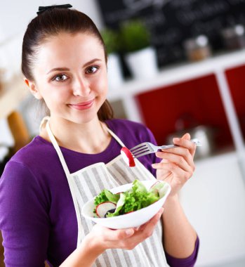 Genç kadın modern mutfakta taze salata yiyor.