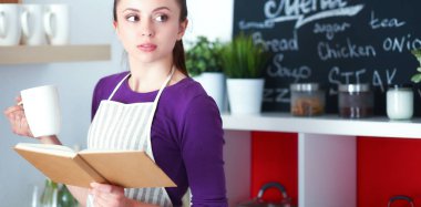 Mutfakta yemek kitabı okuyan genç bir kadın yemek tarifi arıyor.