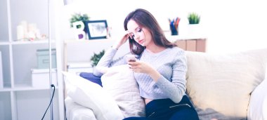 Güzel kız evdeki kanepede akıllı telefonunu kullanıyor.