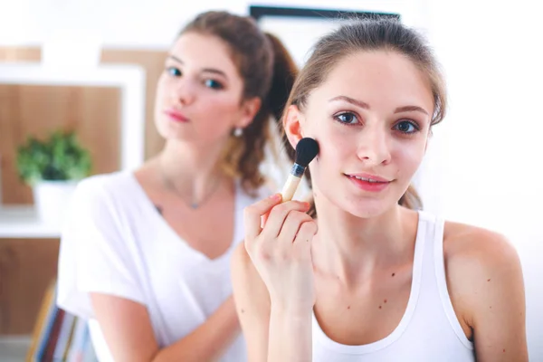 Meninas bonitas olhando no espelho e aplicando cosméticos com uma escova grande — Fotografia de Stock