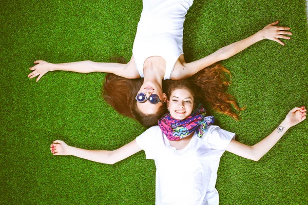 两个漂亮的姑娘躺在鲜绿的草地上 — 图库照片