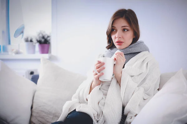 Portrait of a sick woman blowing her nose while sitting on the sofa — Stock Photo, Image