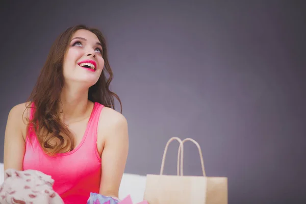 Bella giovane donna seduta a letto con le borse della spesa dopo lo shopping di successo — Foto Stock