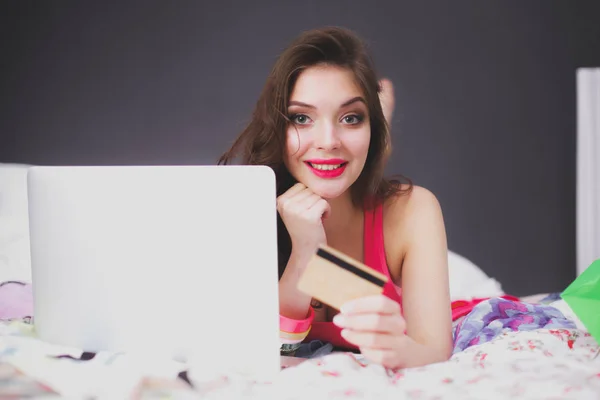 Vacker kvinna liggande på sängen med en laptop och kreditkort — Stockfoto