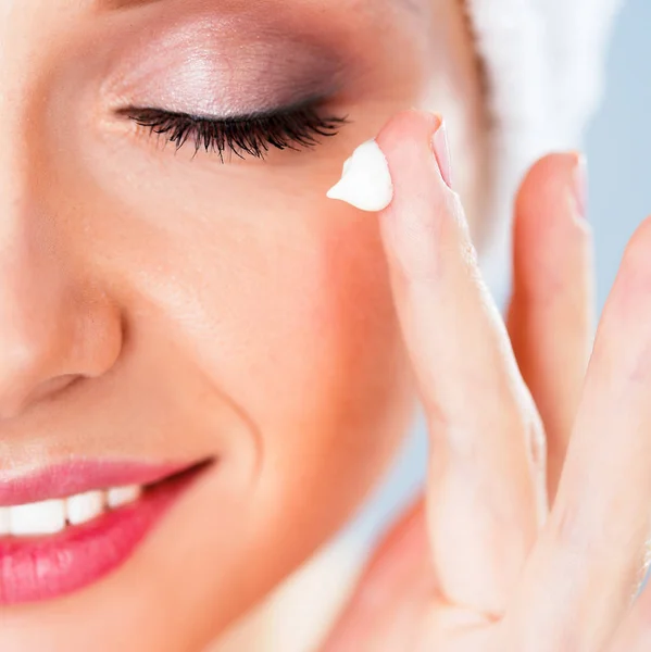 Hermosa joven aplicando una crema en su cara aislada sobre fondo gris — Foto de Stock