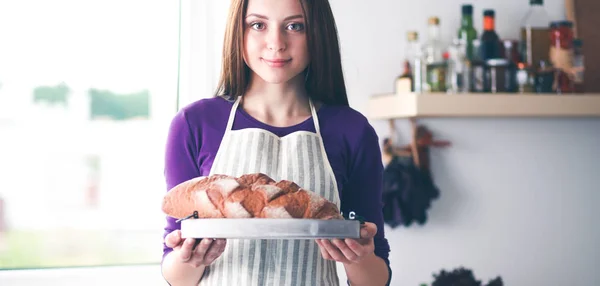 Uma jovem mulher de pé em sua cozinha segurando pão . — Fotografia de Stock