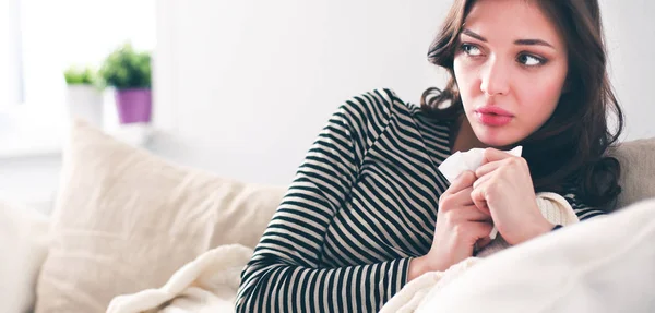 Portrait of a sick woman blowing her nose while sitting on the sofa — Stock Photo, Image