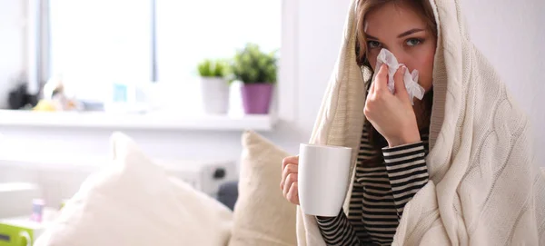 Portrait of a sick woman blowing her nose while sitting on the sofa — Stock Photo, Image