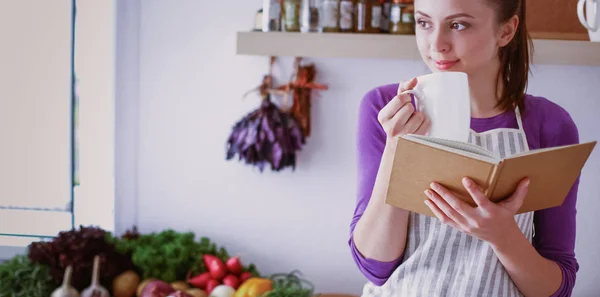 Jonge vrouw die kookboek leest in de keuken, op zoek naar recept — Stockfoto