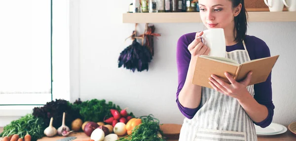 Jonge vrouw die kookboek leest in de keuken, op zoek naar recept — Stockfoto