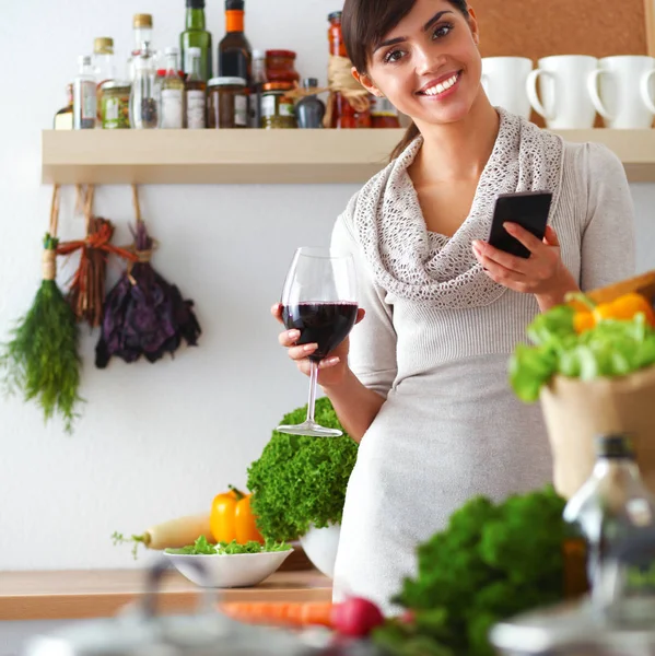 Молодая женщина режет овощи на кухне, держа бокал вина — стоковое фото