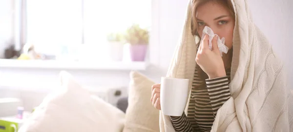 Portrait of a sick woman blowing her nose while sitting on the sofa — Stock Photo, Image