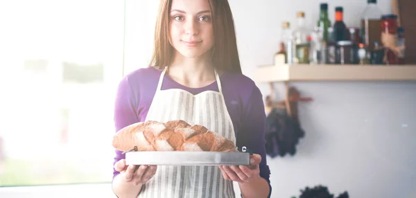 Uma jovem mulher de pé em sua cozinha segurando pão . — Fotografia de Stock