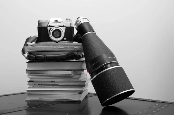 Close-up of analog camera, Photographic roll of film and a Retro Camera Lens stacked on books. old camera over stack of book.  Analog film strips. Analog photography. black and white photo.