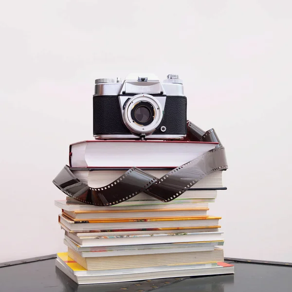 Close-up of analog camera, Photographic roll of film over stack of books. old retro camera stacked on book. Analog film strips. Analog photography.
