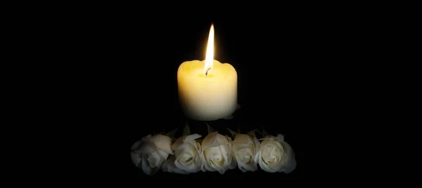 panoramic of White roses and burning candles on table in darkness, Copy space for text. candles burning in the black background. Funeral symbol. The concept of mourn, grief or mourning.