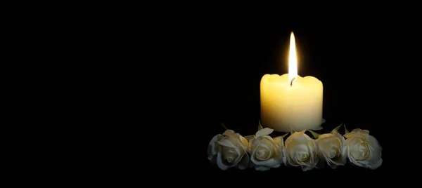panoramic of White roses and burning candles on table in darkness, Copy space for text. candles burning in the black background. Funeral symbol. The concept of mourn, grief or mourning.