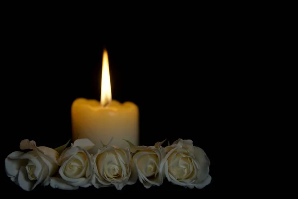 White roses and burning candles on table in darkness, Copy space for text. candles burning in the black background. Funeral symbol. The concept of mourn, grief or mourning.