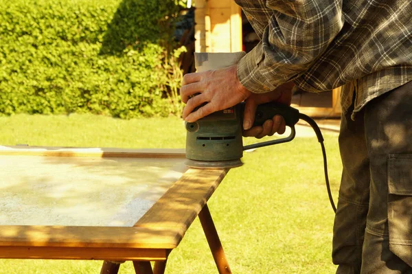 preparation grinding woodwork outside. Close-up details of Male hand sanding a door with a random orbital sander in spring. Concept of renovation works, Carpentry details with woodwork and handyman