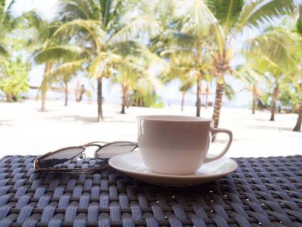 A cup of black coffee and sun glasses with coconut tree plan on white sand beach sea view background, Travel plans after retirement of business people