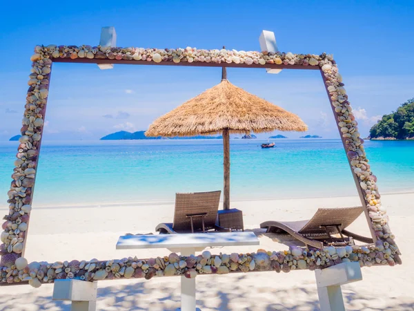 有蓝色海景背景的相框中的白色沙滩上的阳光遮蔽处，假日或退休后的旅行计划 — 图库照片
