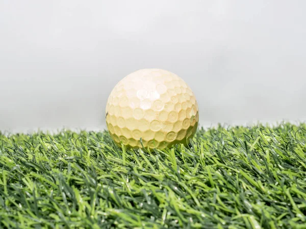 Foto de bola de golfe amarelo na grama artificial com fundo branco — Fotografia de Stock