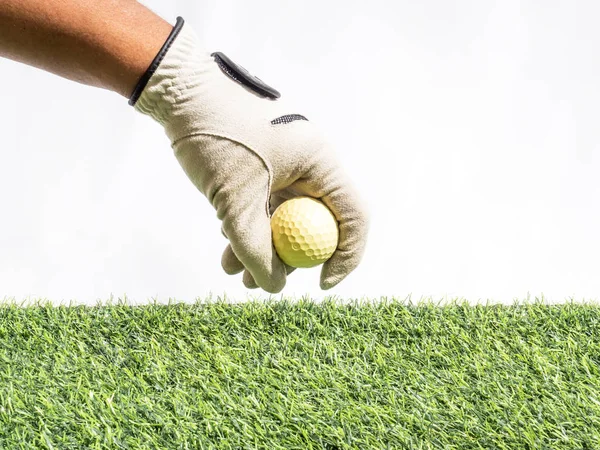 Φωτογραφία από ένα χέρι Τοποθέτηση κίτρινο μπάλα του γκολφ τεχνητό γρασίδι με λευκό φόντο — Φωτογραφία Αρχείου