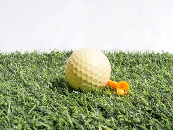 Foto de bola de golfe amarelo e tee laranja na grama artificial com fundo branco — Fotografia de Stock