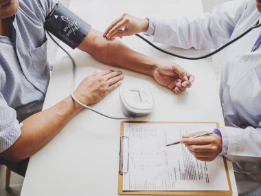 Doktor hastayı steteskopla, tansiyon monitörüyle muayene eder ve sonuçları kaydeder.
