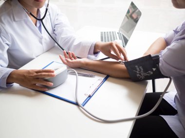 Doktor hastayı steteskopla, tansiyon monitörüyle muayene eder ve sonuçları kaydeder.