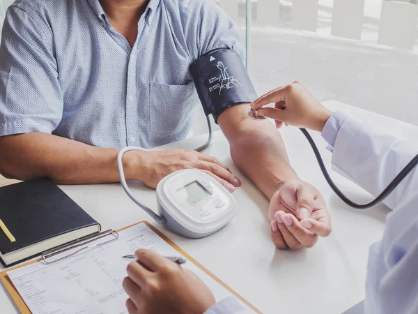 El médico evalúa al paciente con un estetoscopio, un monitor de presión arterial y registra los resultados — Foto de Stock