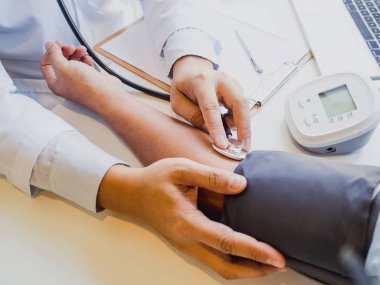 Doktor hastayı steteskopla, tansiyon monitörüyle muayene eder ve sonuçları kaydeder.