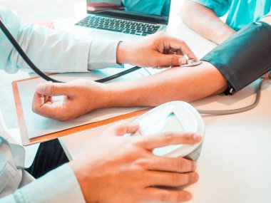 Doktor hastayı steteskopla, tansiyon monitörüyle muayene eder ve sonuçları kaydeder.