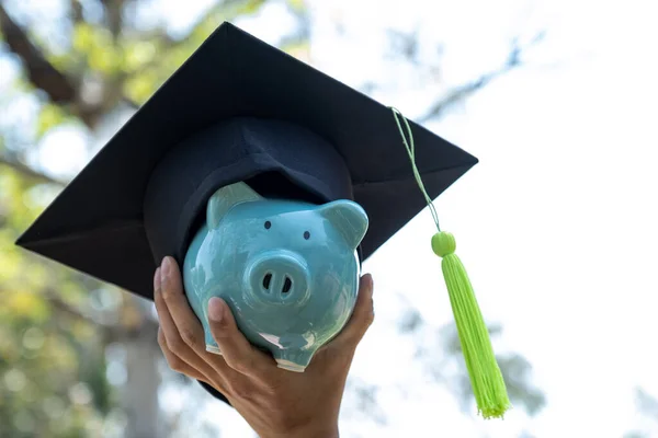 手持印有毕业帽的蓝色储蓄罐 为教育计划和退休基金概念存钱 — 图库照片