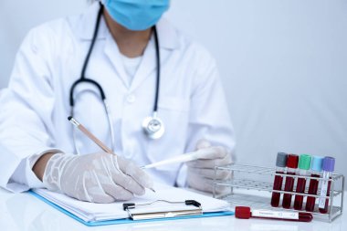 Doktor eli kan tüpü tutuyor ve kan testinin sonuçlarını kaydediyor..