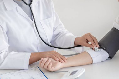 Doktor, hastayı steteskopla, tansiyon monitörüyle muayene eder ve sonuçları kaydeder..