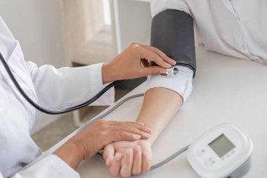 Doktor, hastayı steteskopla, tansiyon monitörüyle muayene eder ve sonuçları kaydeder..