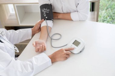 Doktor, hastayı steteskopla, tansiyon monitörüyle muayene eder ve sonuçları kaydeder..