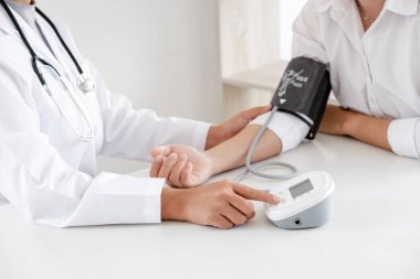 Doktor, hastayı steteskopla, tansiyon monitörüyle muayene eder ve sonuçları kaydeder..