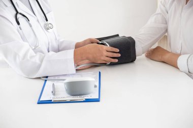 Doktor, hastayı steteskopla, tansiyon monitörüyle muayene eder ve sonuçları kaydeder..