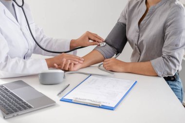 Doktor, hastayı steteskopla, tansiyon monitörüyle muayene eder ve sonuçları kaydeder..